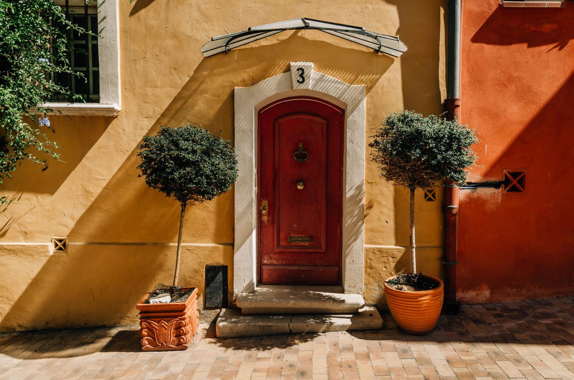 porte rouge baignée de lumière avec deux pots de plantes autour dans une ruelle colorée de Cassis, près de Marseille