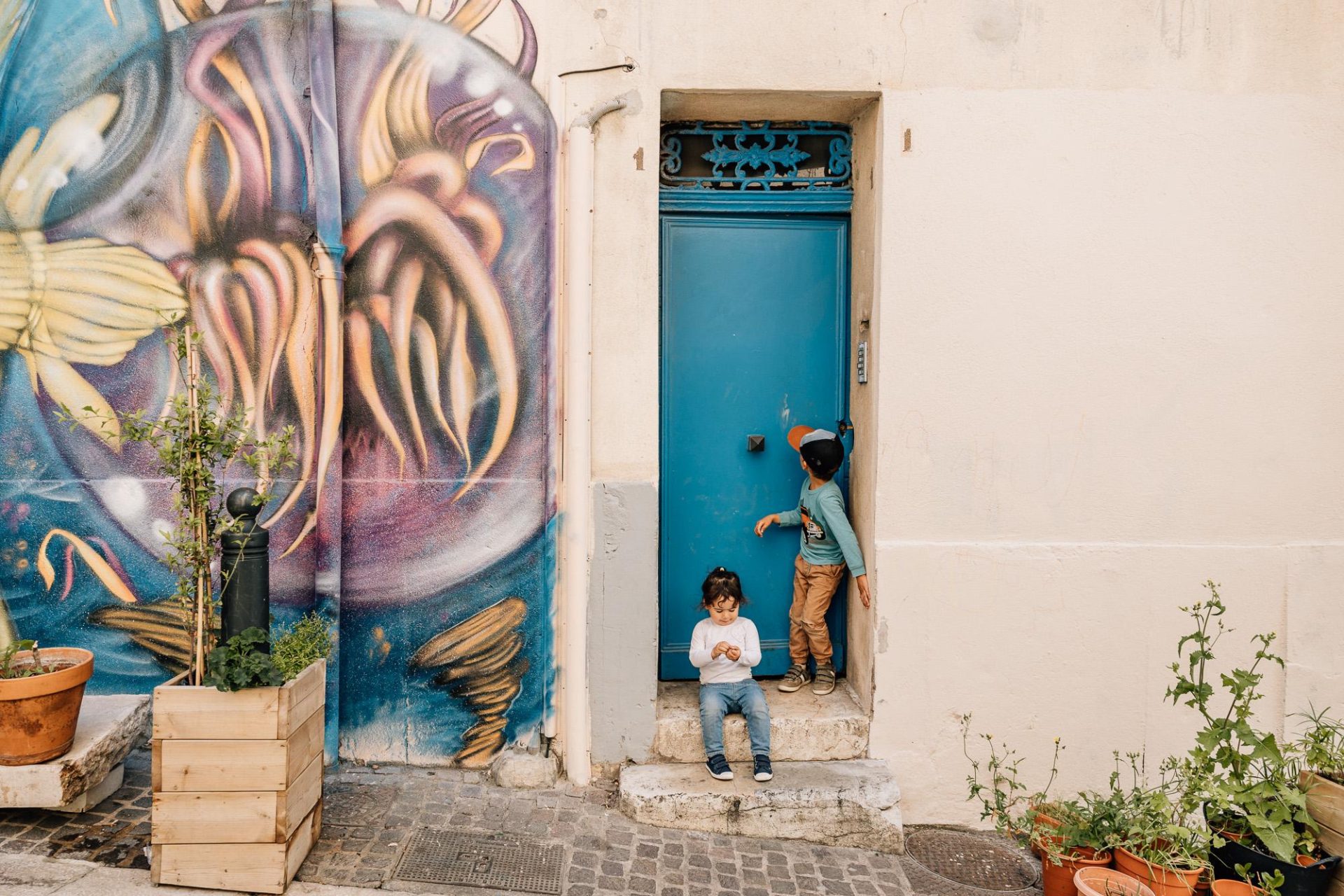 Enfants devant une porte bleue à côté d'une superbe murale dans le quartier du Panier à Marseille pendant une séance photo de famille