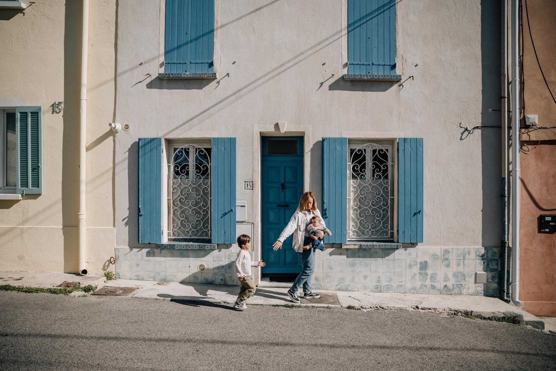 maman marche avec ses deux enfants devant une maison blanche et bleue à Malmousque lors d'une séance photo famille à Marseille