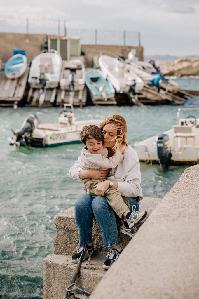 maman assise avec son petit garçon dans les bras au Port de Malmousque pendant une séance photo de famille à Marseille