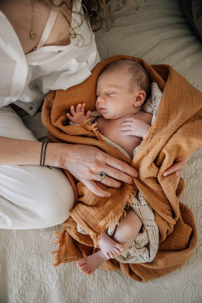 Nouveau-né dort paisiblement dans une couverture auprès de sa maman, lors d'une séance photo nouveau-né authentique et naturelle à domicile à Marseille. Idée originale pour les faire-parts de naissance.
