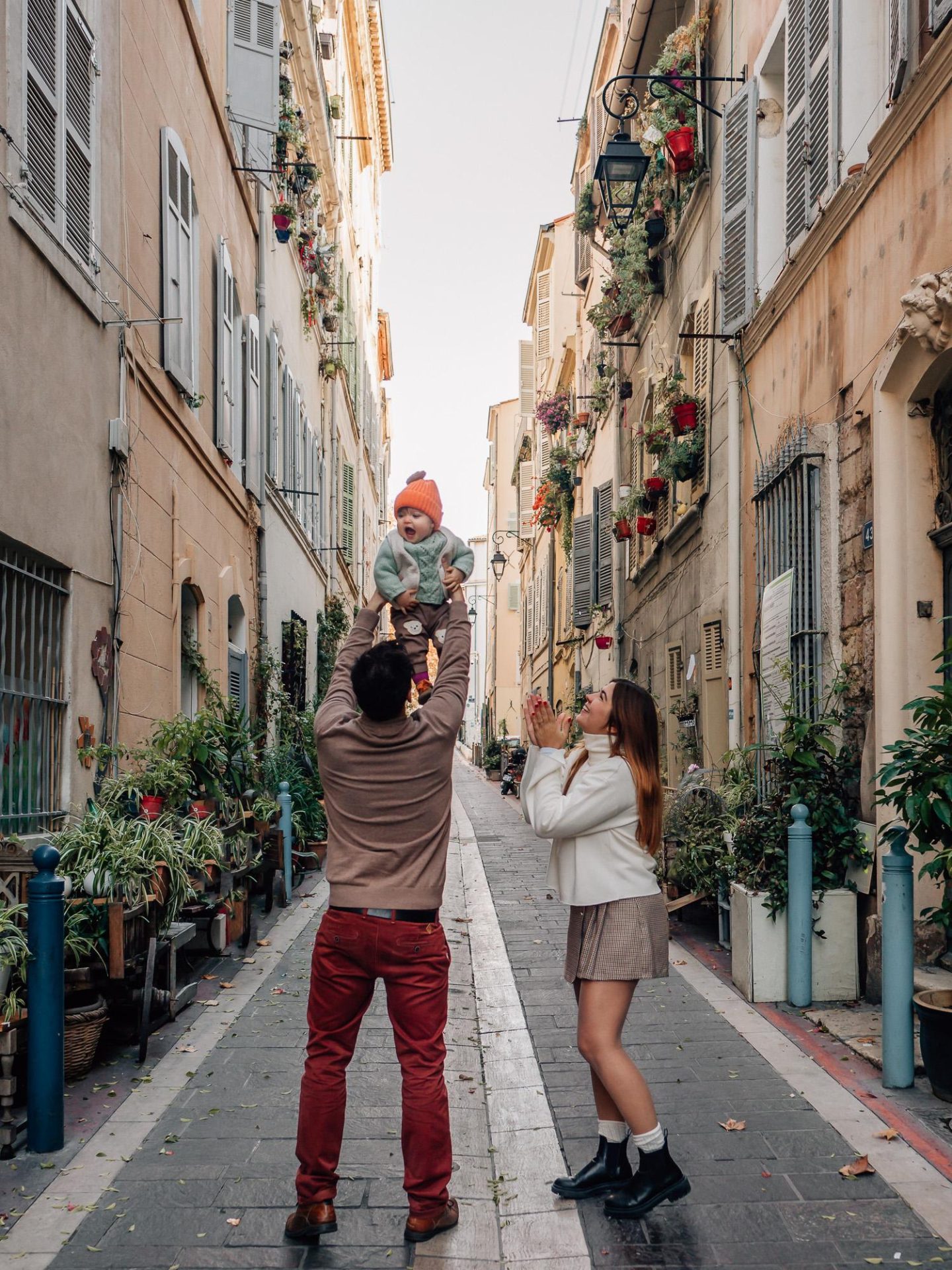 scène de jeu et de bonheur : parents qui lancent leur petite fille dans les airs qui rit aux éclats pendant un shooting photo famille dans les rues du Panier à Marseille