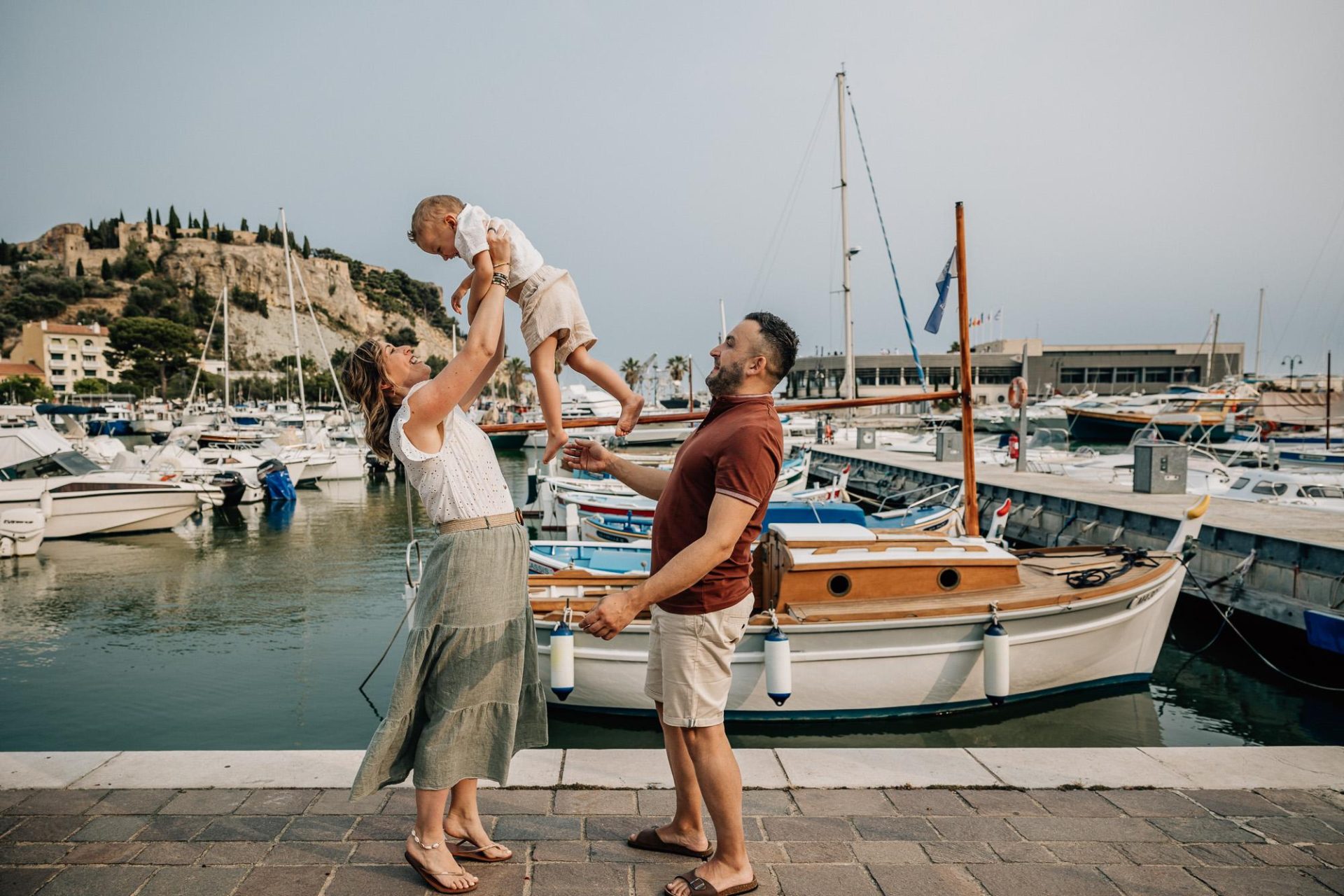 les parents et leur petit garçon jouent lors d'une séance photo de famille au port de Cassis