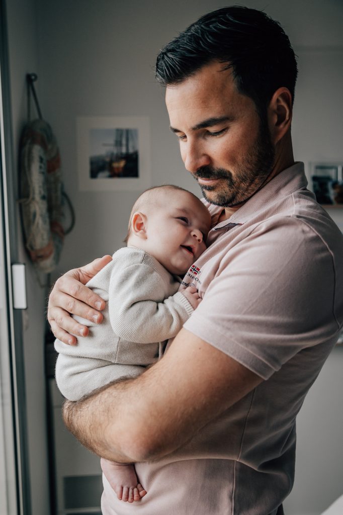 portrait d'un père regardant tendrement son nouveau-né qu'il porte dans les bras pendant un shooting photo nouveau-né à domicile à Marseille
