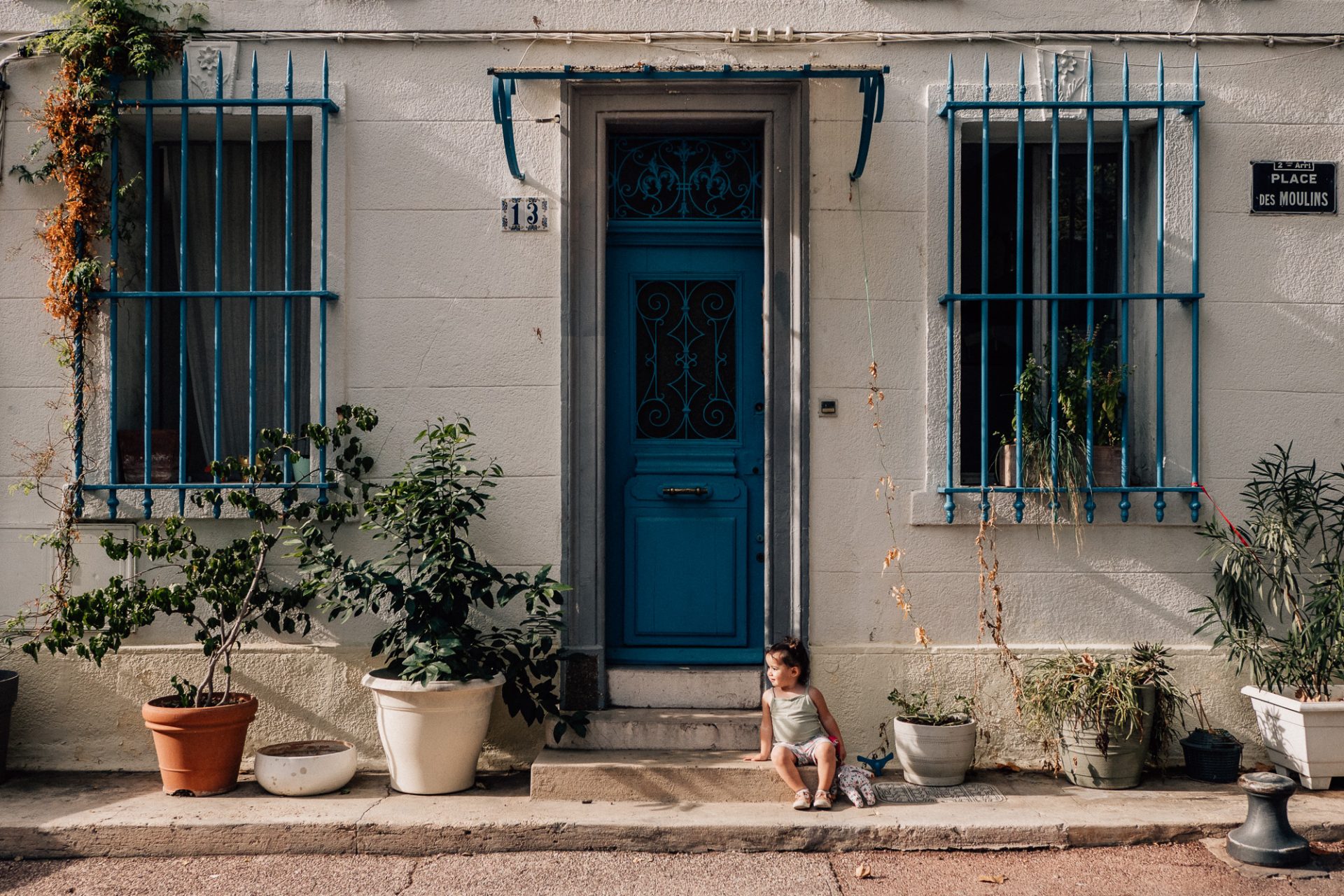 petite fille posant lors d'une séance photo lifestyle dans le quartier du Panier à Marseille devant une jolie maison avec une porte bleue et des plantes