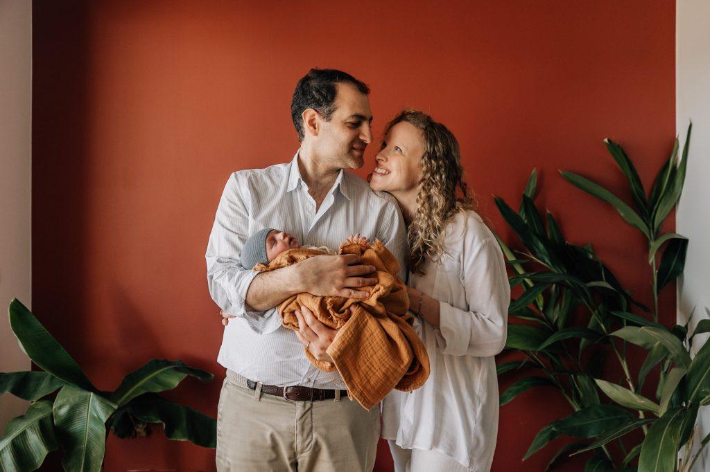 Les nouveaux parents se regardent tendrement alors que bébé est dans les bras de son papa lors d'un shooting photo nouveau-né à domicile à Marseille