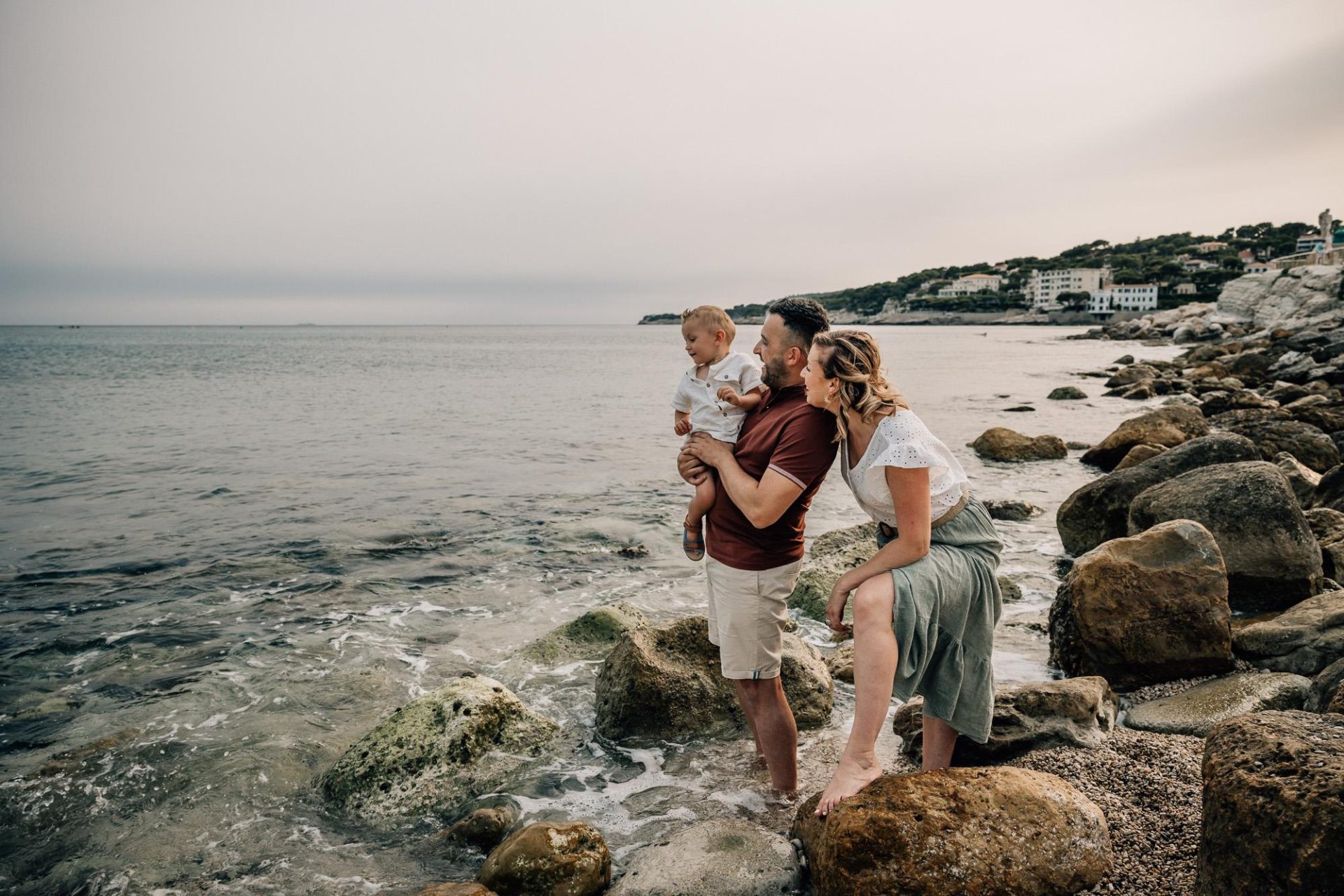 les parents et leur petit garçon sont heureux et rient lors d'une séance photo de famille à la plage à Cassis