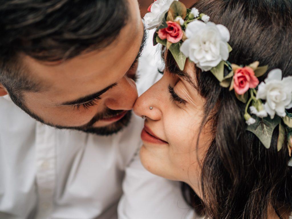 portrait serré d'un couple de jeunes mariés qui s'embrassent lors d'une séance photo de couple. Une couronne de fleurs est posée sur la tête de la jeune femme