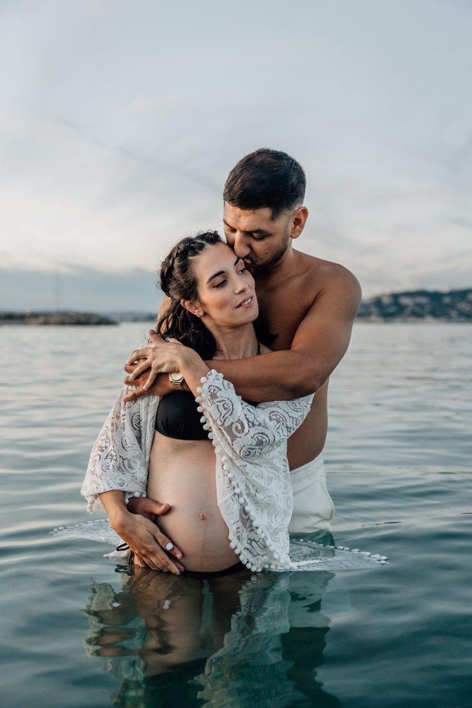 moment de tendresse d'un couple lors d'un shooting photo de grossesse dans l'eau de la plage de la Pointe Rouge à Marseille