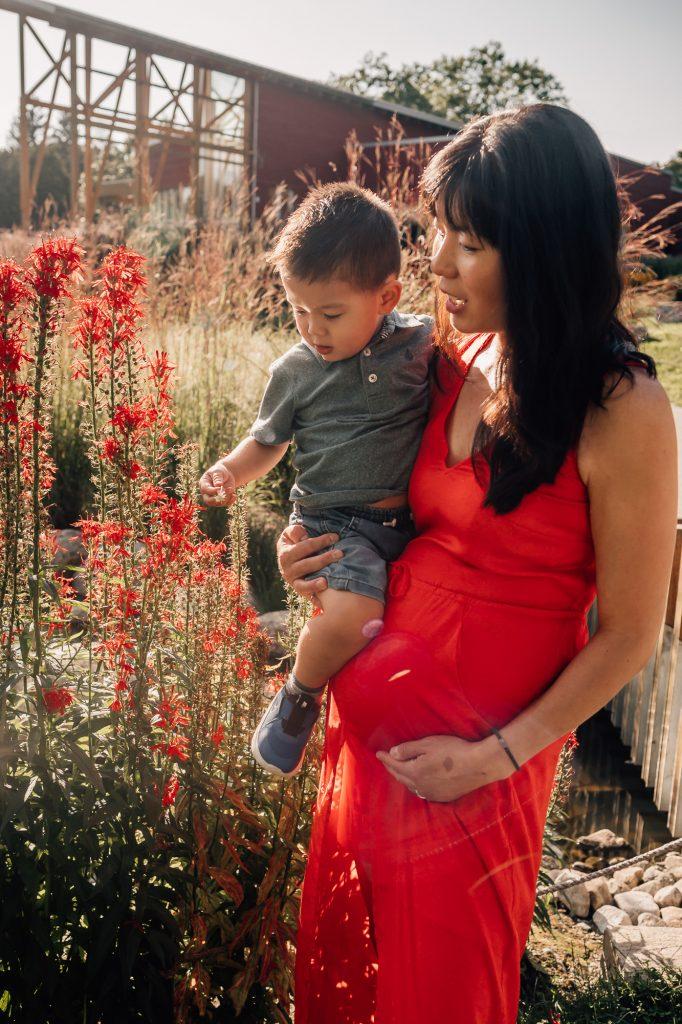 femme enceinte dans une robe rouge porte son petit garçon dans les bras au milieu des fleurs lors d'une séance photo de grossesse en Provence