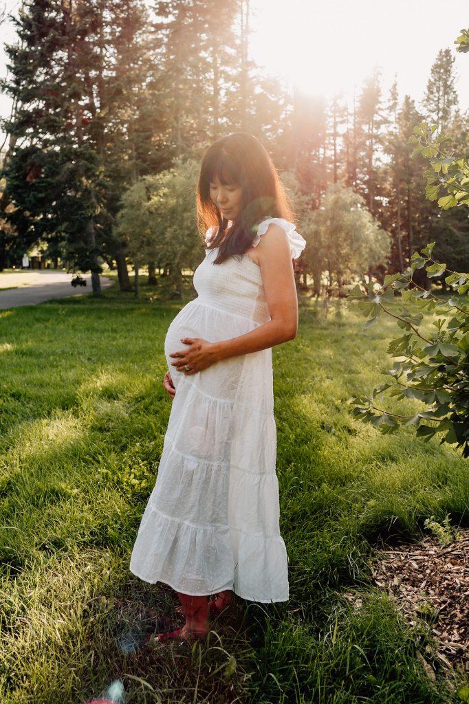 femme enceinte dans une robe blanche pose dans un parc lors d'une séance photo de grossesse en Provence