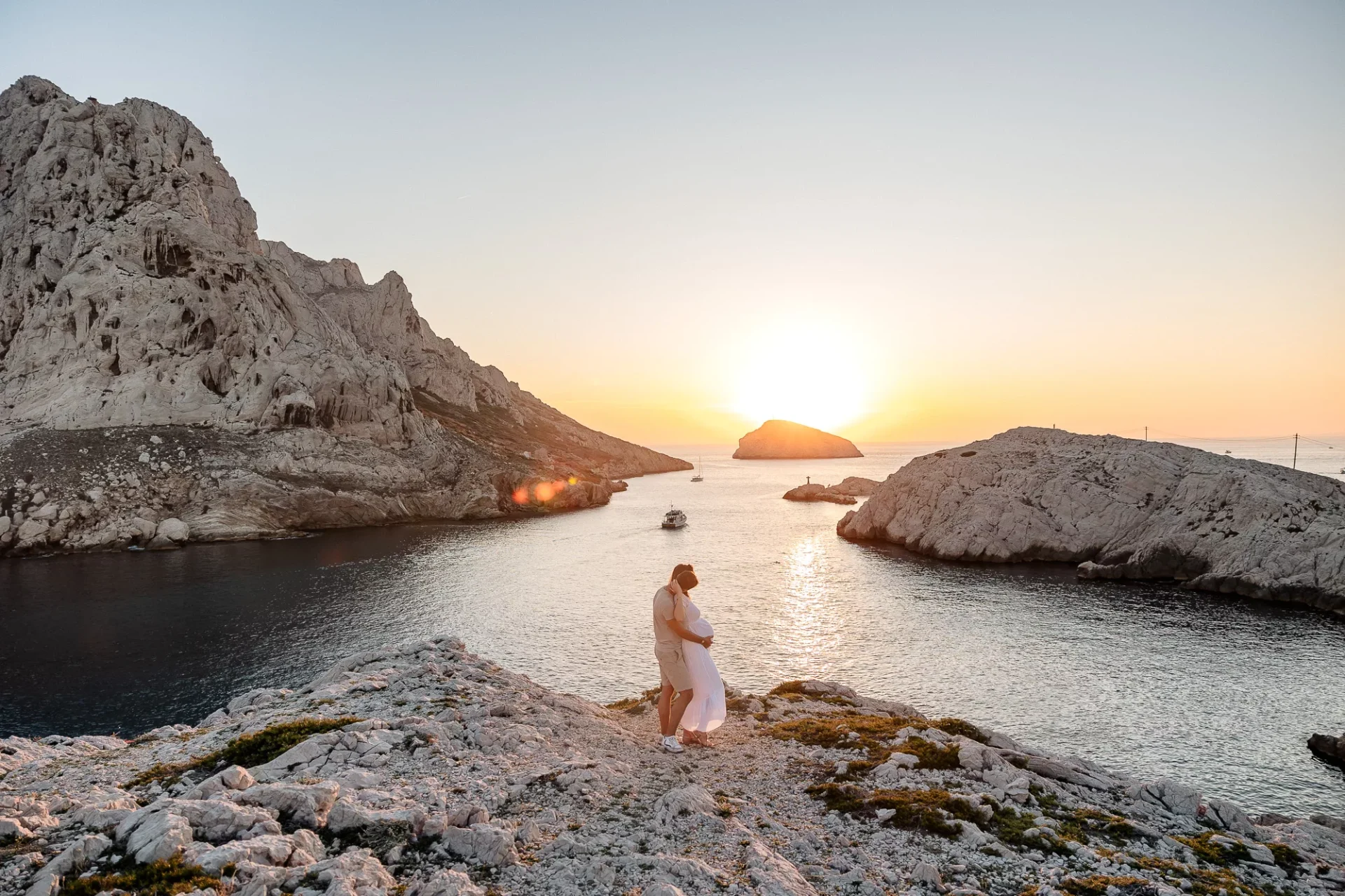 Couple enlacé sur un rocher face à la mer lors d’une séance photo grossesse dans les calanques des Goudes de Marseille au coucher du soleil