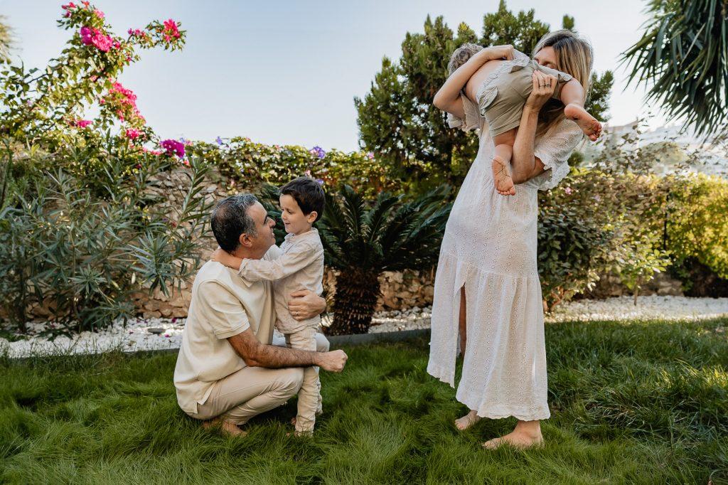 maman et papa jouent avec leurs deux petits garçons dans le jardin. Ils sont tous habillés dans des tons beiges dans un style chic-bohème