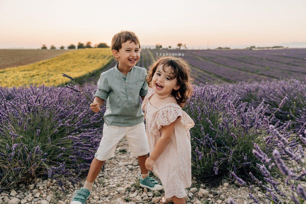 un frère et sa soeur heureux dans un champ de lavande lors d'une séance photo au Plateau de Valensole avec une photographe de famille basée à Marseille