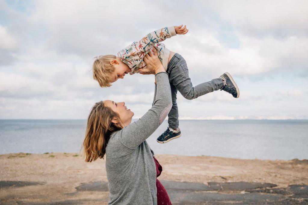 maman enceinte lance son fils dans les airs lors d'un shooting photo lifestyle naturel de grossesse en extérieur à Marseille