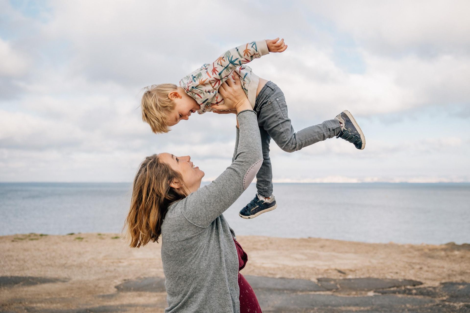 maman enceinte lance son fils dans les airs lors d'un shooting photo lifestyle naturel de grossesse en extérieur à Marseille