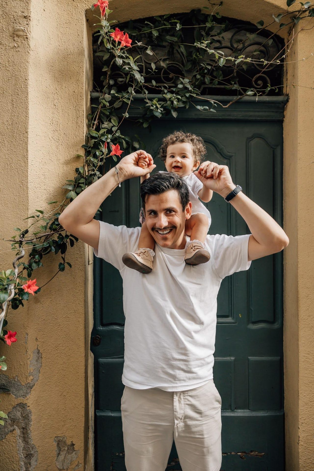 papa porte sa petite fille devant une jolie porte en fleur lors d'une séance photo famille au Panier à Marseille