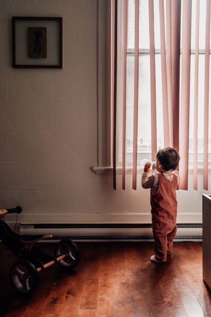 petite fille avec son biberon regarde la fenêtre depuis la salon lors d'une séance photo à domicile à Marseille