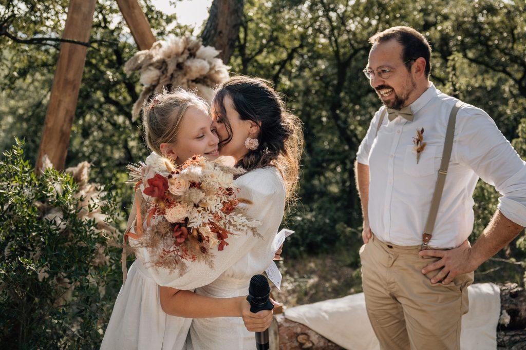 Mariée tenant un bouquet enlace sa fille lors d’une cérémonie laïque d'un mariage en extérieur à Aix-en-Provence
