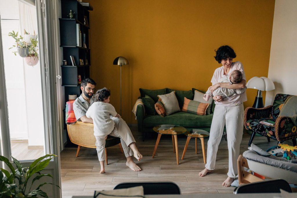 maman avec bébé dans les bras et papa joue avec sa fille lors d'une séance photo à domicile à Marseille