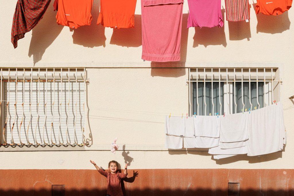 Enfant jetant son doudou devant une façade colorée où du linge rose est étendu dans une ruelle à Marseille