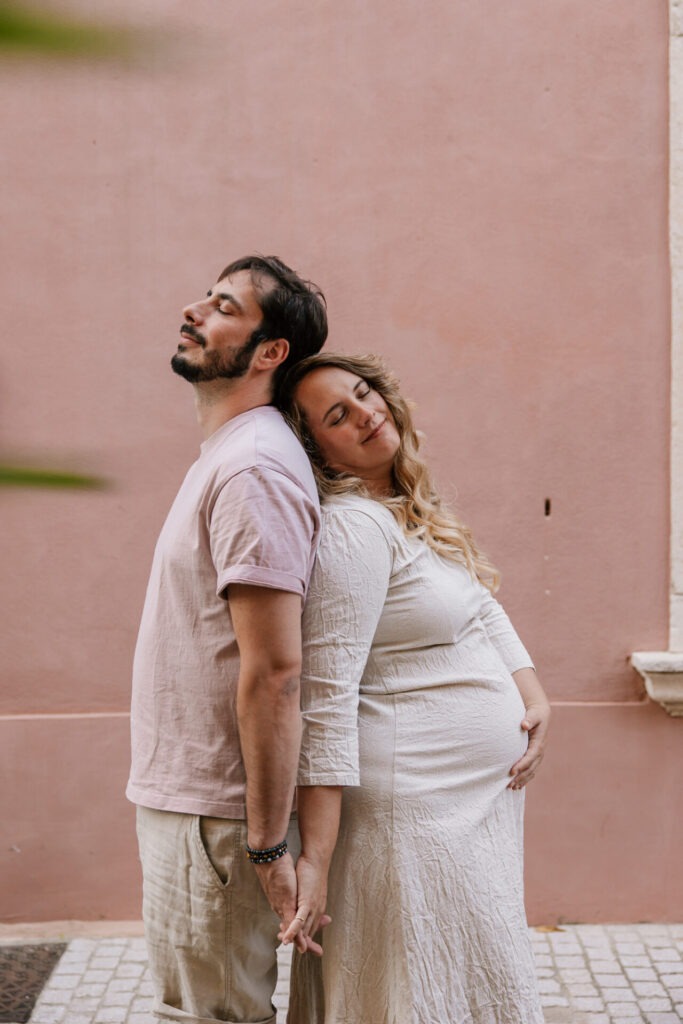 Couple dos à dos lors d'une séance photo grossesse couple à Cassis devant façade rose pastel
