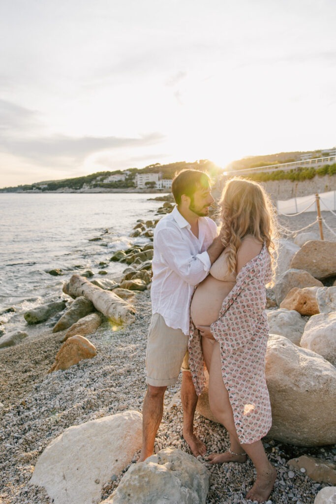 Couple s'embrasse lors d'une séance photo grossesse à Cassis au coucher du soleil sur la plage et les rochers