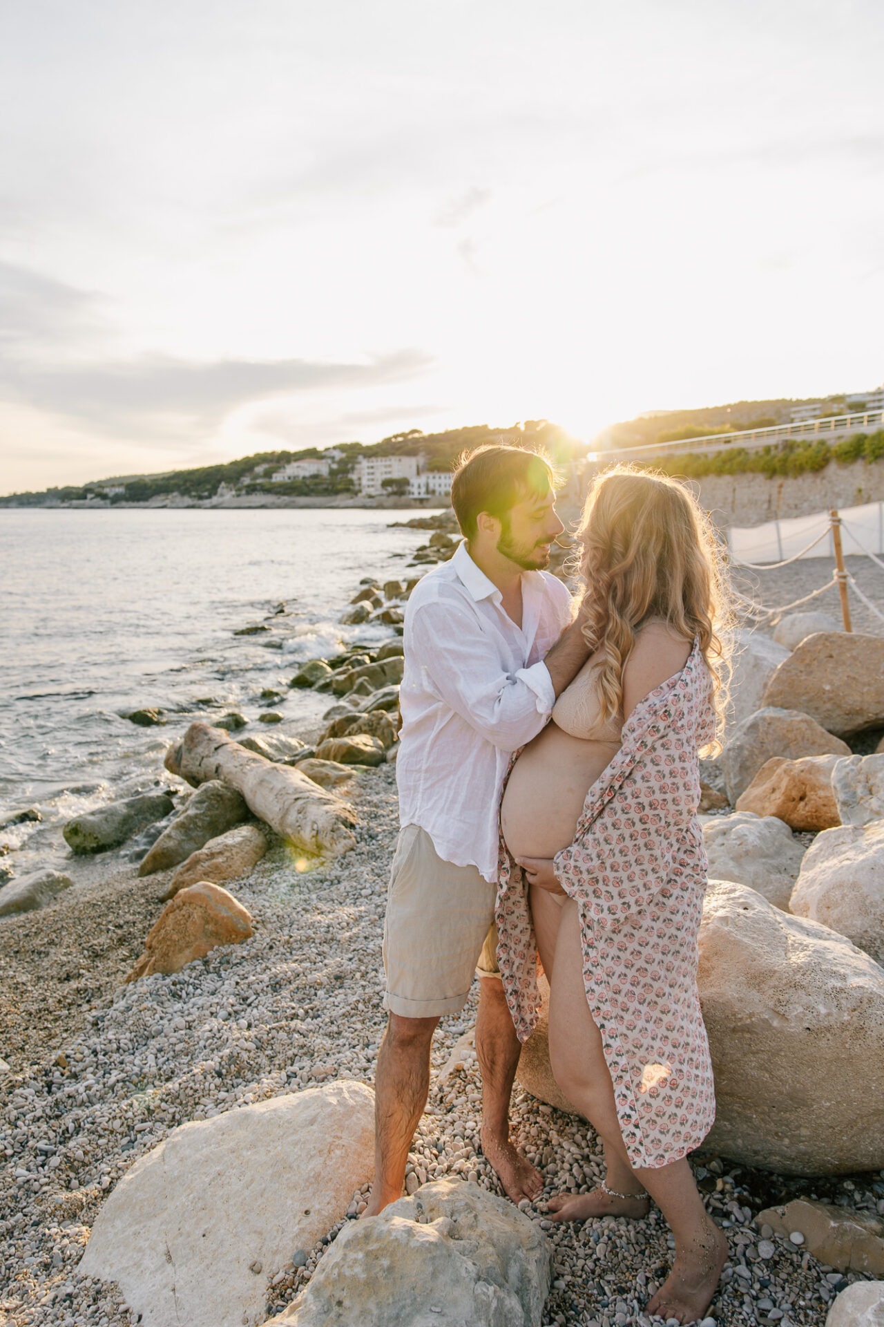 Couple s'embrasse lors d'une séance photo grossesse à Cassis au coucher du soleil sur la plage et les rochers