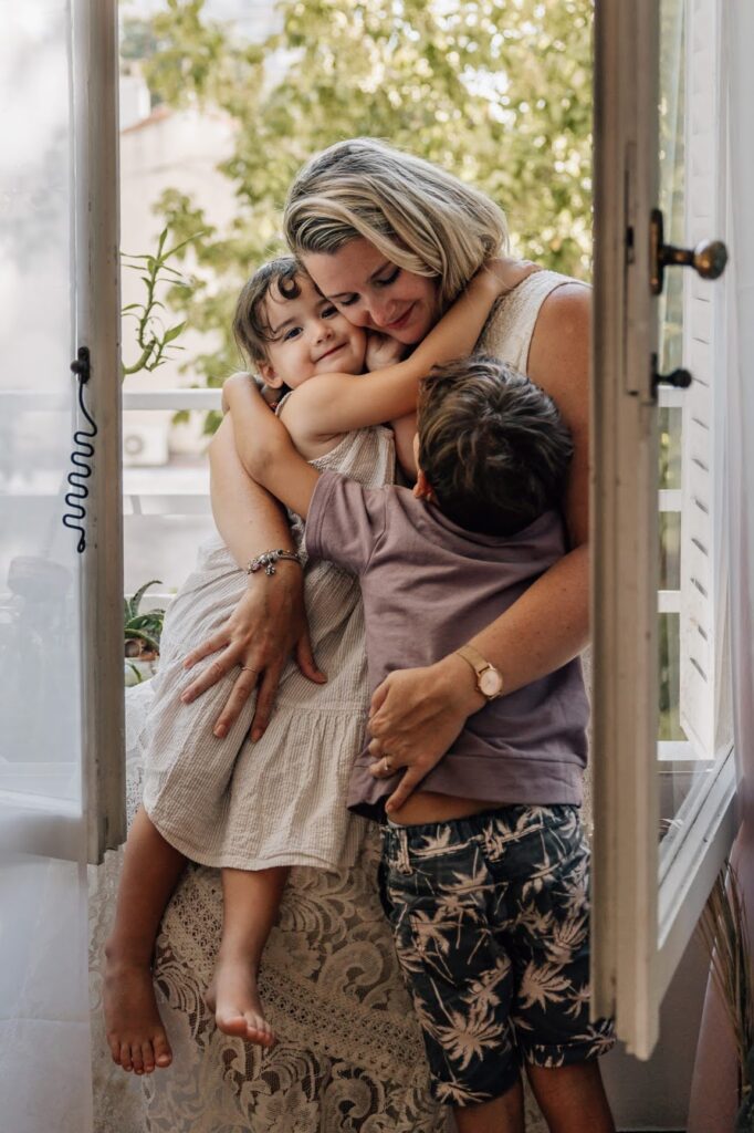 Maman avec ses enfants près d’une fenêtre – séance photo famille à domicile à Marseille