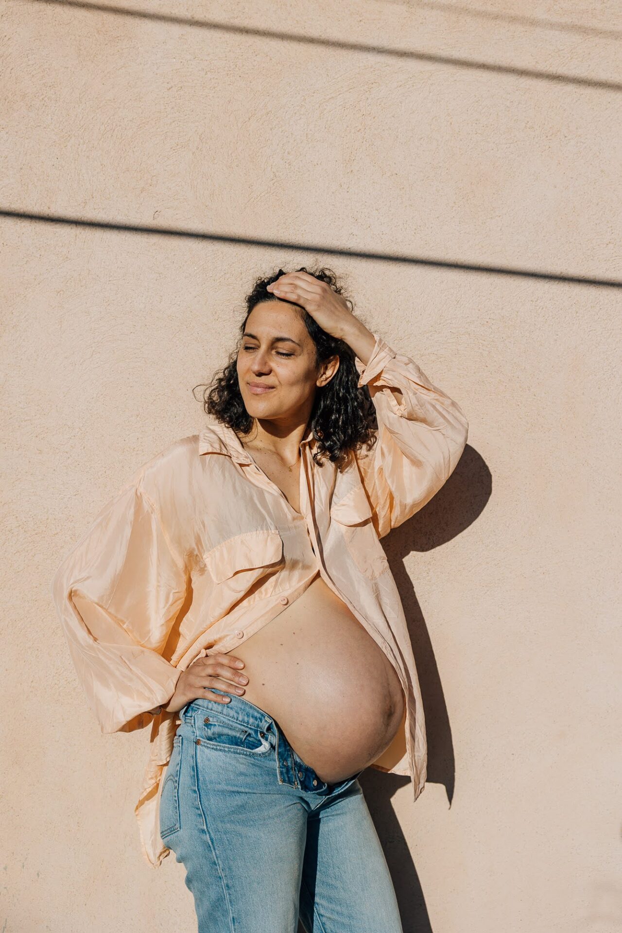 portrait minimaliste d'une femme enceinte habillée en chemise et jean devant un mur coloré avec des lignes graphiques lors d'une séance photo en ville à Marseille