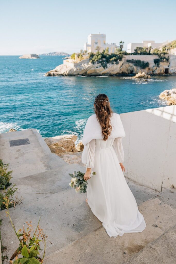 Mariée marchant au bord de l'eau sur la côte marseillaise lors d'une journée ensoleillée