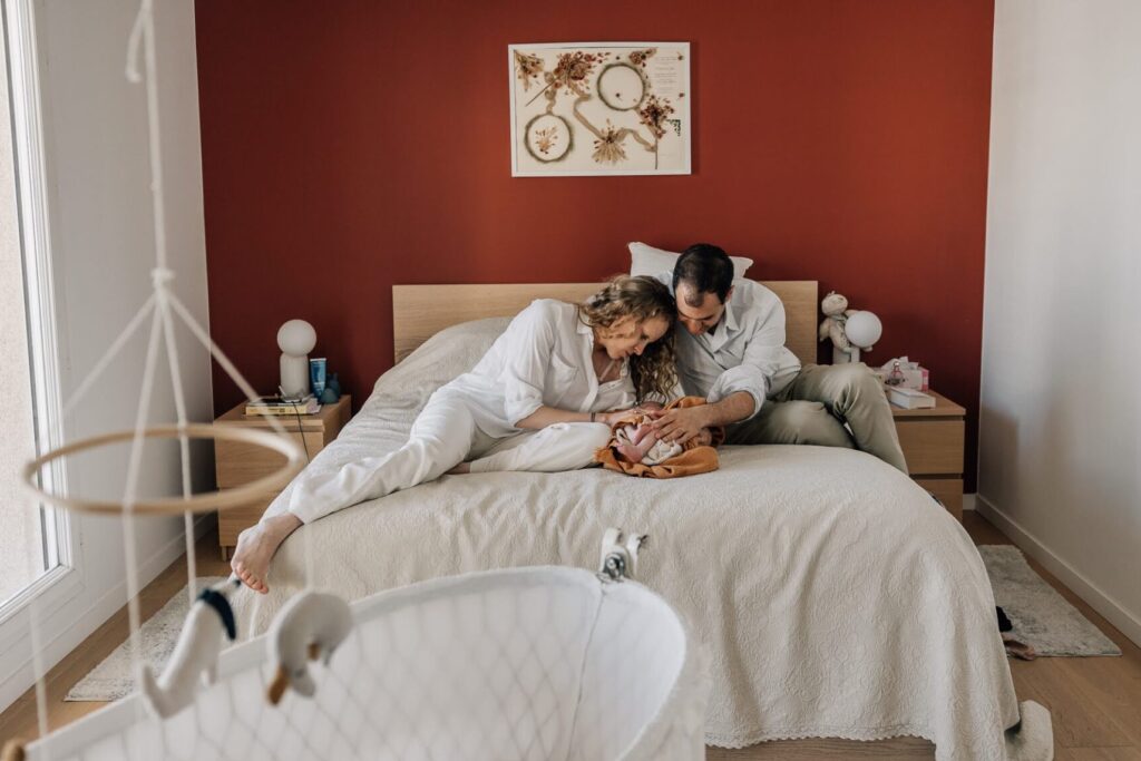 Parents allongés avec leur nouveau-né sur un lit lors d’une séance photo bébé à domicile à Marseille