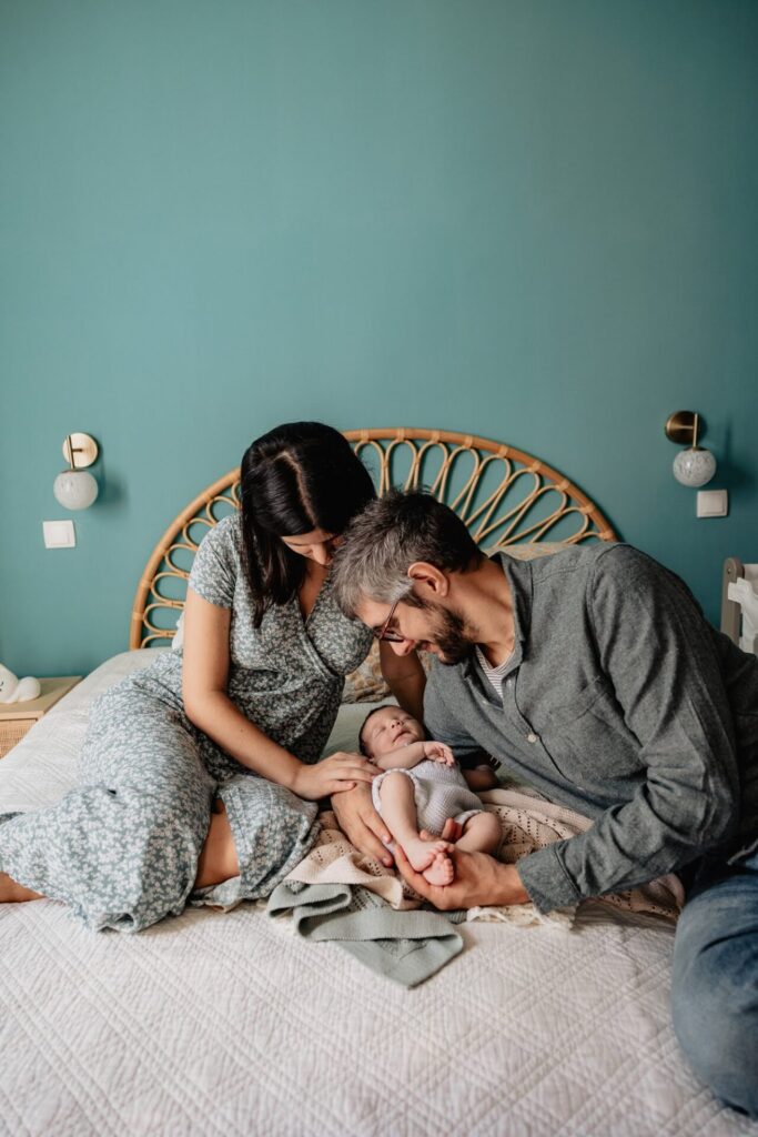 Parents assis sur un lit avec leur nouveau-né lors d’une séance photo bébé à domicile à Marseille 13008