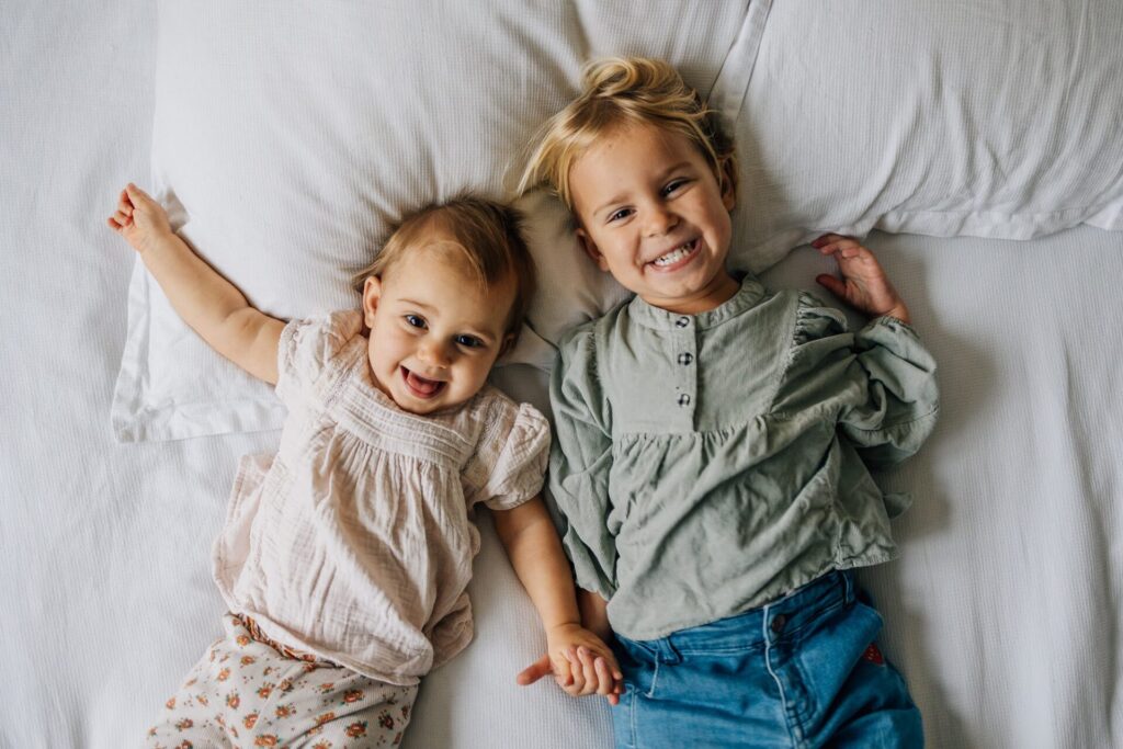 Bébé et sa grande soeur souriant à la caméra lors d'une séance photo famille à domicile à Marseille 13009