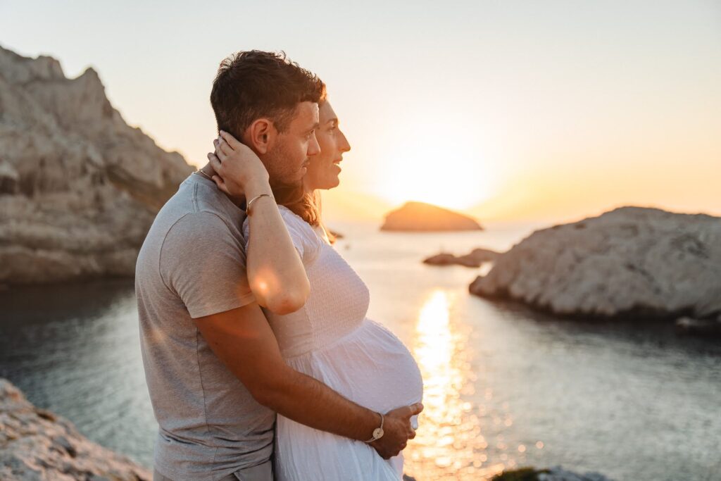 Couple au coucher du soleil lors d’une séance grossesse en bord de mer aux Goudes à Marseille