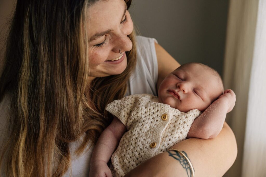 Maman tenant son bébé contre elle pendant une séance photo nouveau-né à domicile à Marseille