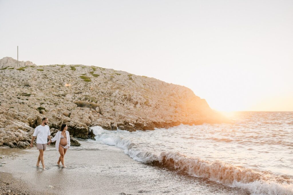 Couple marchant au bord de l’eau au coucher du soleil pendant une séance grossesse aux Goudes à Marseille 13008