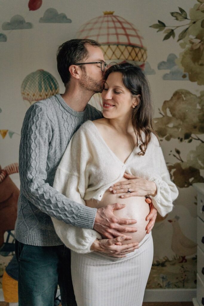 Couple enlacé dans la chambre de leur bébé lors d'une séance photo de grossesse à la maison à Marseille