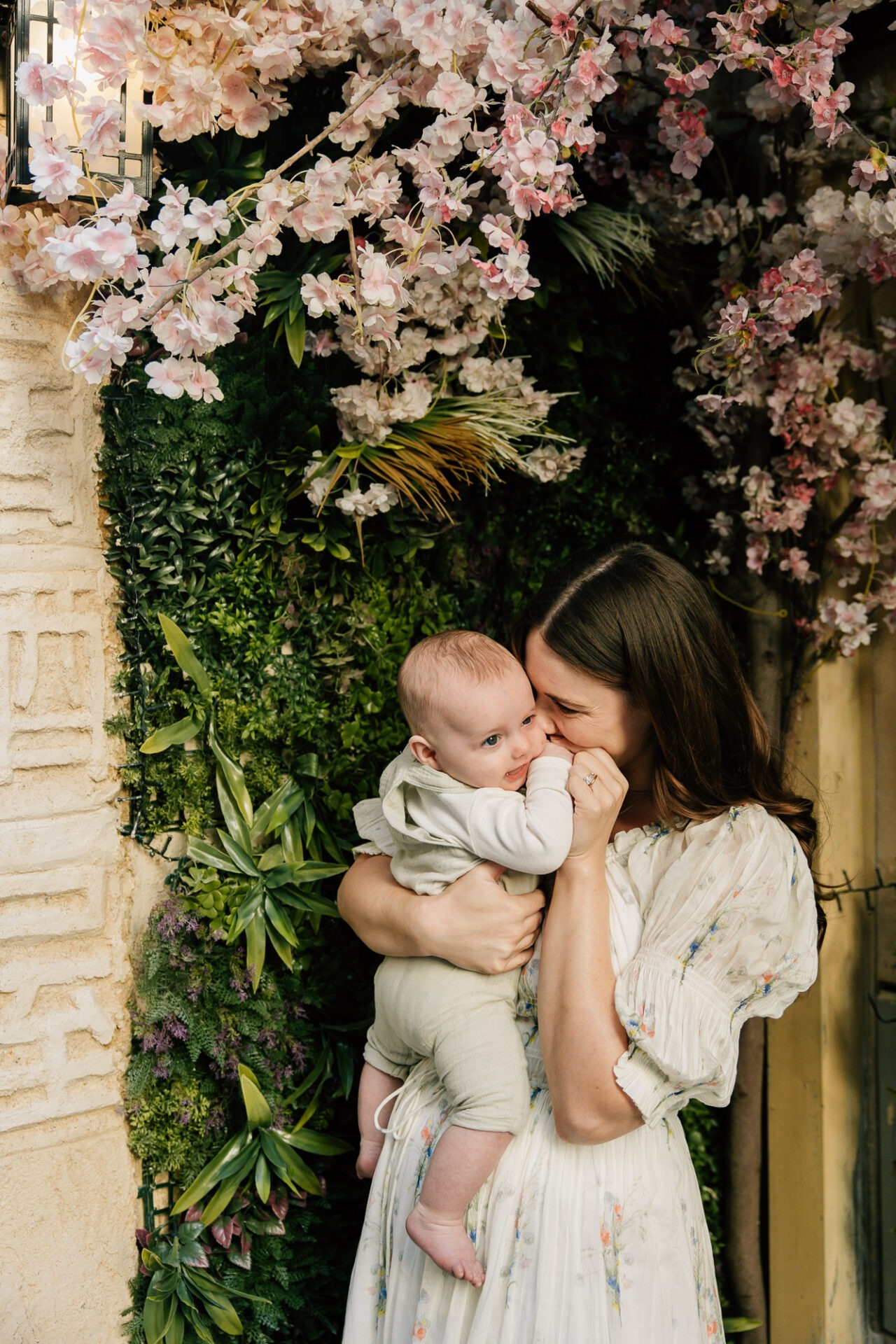 maman embrassant son bébé devant un mur fleuri moment tendre extérieur