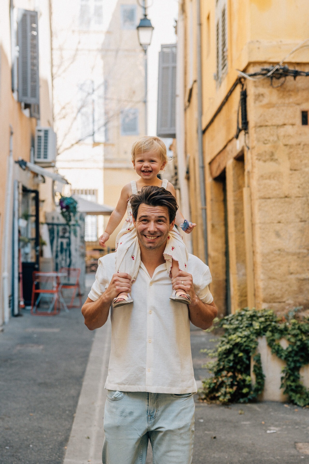 père portant son enfant sur les épaules dans une rue d’aix en provence lumière douce