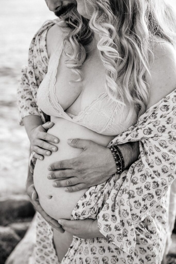 détail du ventre d’une femme enceinte enlacée par son partenaire pendant une séance photo grossesse