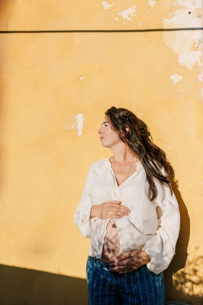 Femme enceinte en chemise blanche et jean devant un mur jaune lors d’une séance grossesse à Marseille