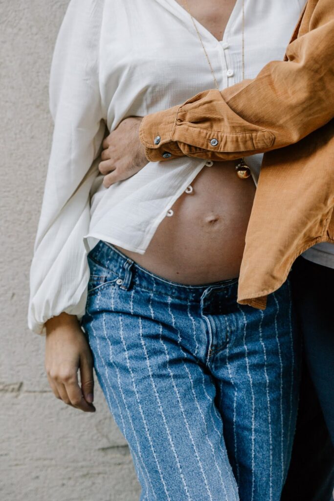 détail du ventre d’une femme enceinte enlacée par son partenaire lors d’une séance photo grossesse