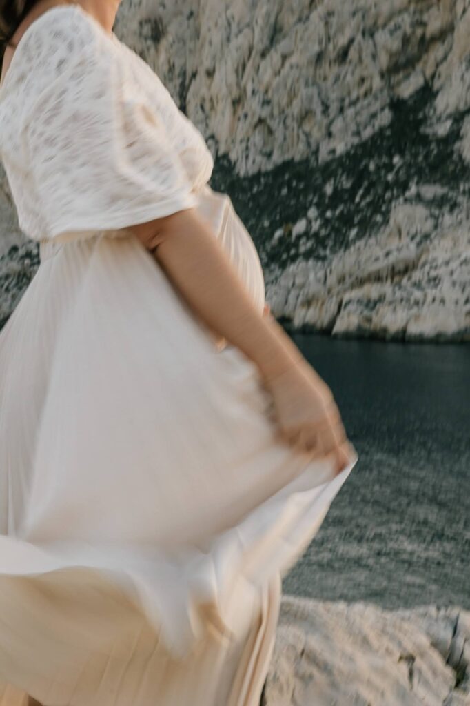 femme enceinte marchant en robe près de la mer lors d’une séance photo grossesse