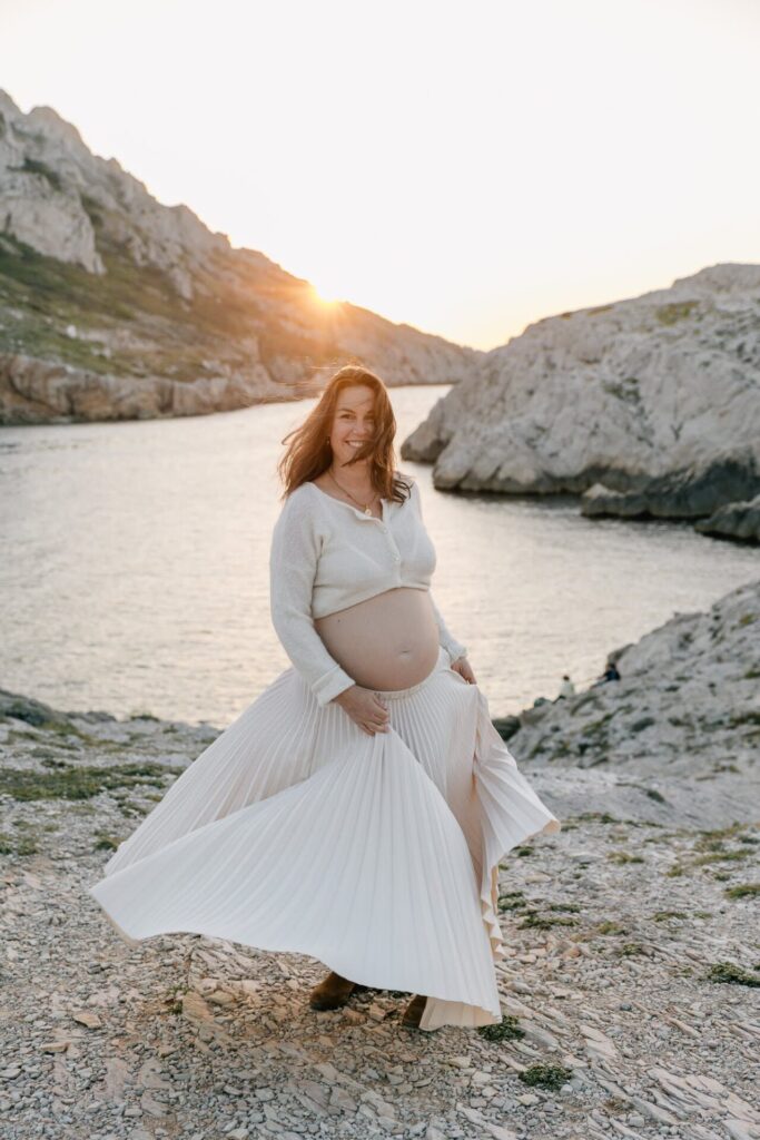 Femme enceinte en robe fluide dansant dans les Goudes au coucher du soleil à Marseille
