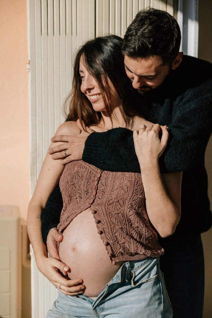 Couple enlacé mettant en valeur un ventre arrondi lors d’une séance grossesse à domicile à Aix en Provence