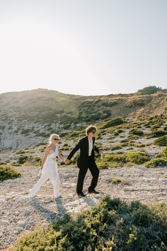 Couple en tenue de mariage marchant main dans la main sur un sentier rocheux lors d'un elopement dans les Calanques de Marseille