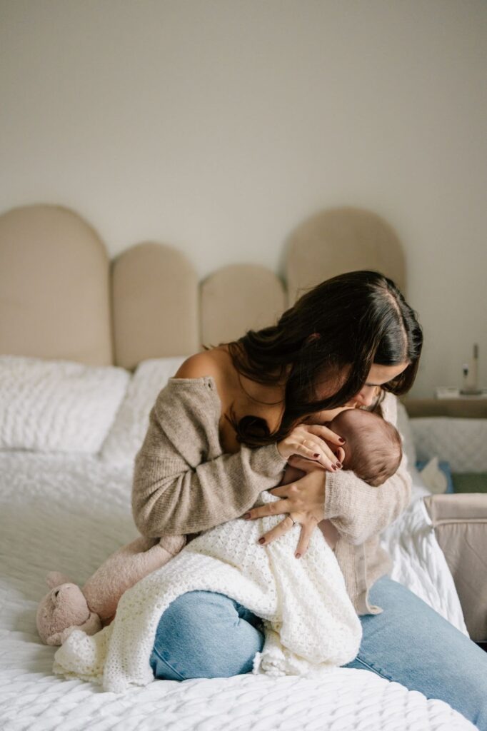 Maman embrassant son nouveau-né sur un lit lors d’une séance photo naissance à domicile à Allauch