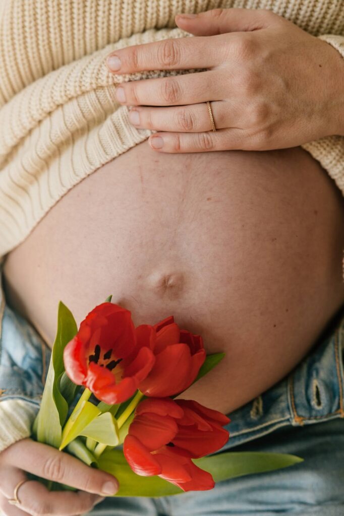 Gros plan du ventre d’une femme enceinte avec une tulipe rouge lors d’une séance grossesse à domicile à Aix-en-Provence