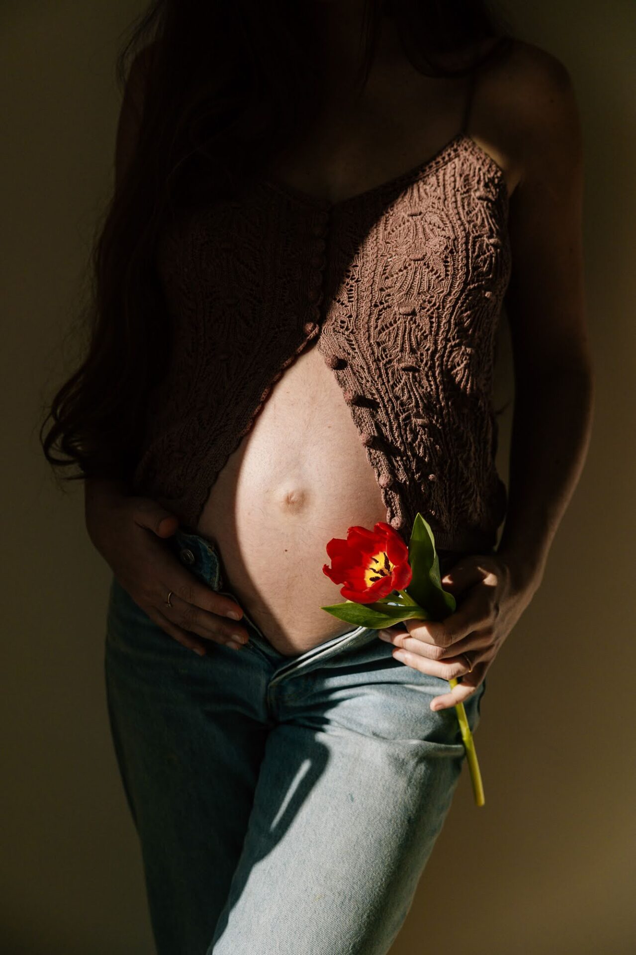 Gros plan du ventre de femme enceinte avec une tulipe rouge, séance grossesse à domicile à Aix-en-Provence